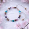 Handgeknoopte armband met bruin/beige koord, gekleurde howliet, bergkristal, jaspis, amehist, rozenkwarts en witte en roze rhinestone kralen.