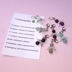 Zeven donkerzilverkleurige hangertjes met geluksengeltjes van edelstenen, met bijbehorend kaartje waarop de eigenschappen van de stenen staan beschreven.