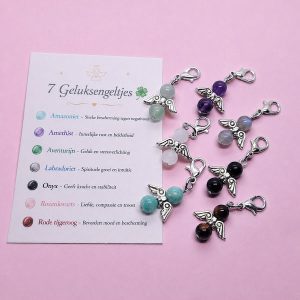 Zeven donkerzilverkleurige hangertjes met geluksengeltjes van edelstenen, met bijbehorend kaartje waarop de eigenschappen van de stenen staan beschreven.