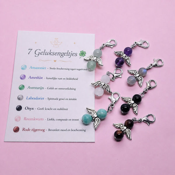 Zeven donkerzilverkleurige hangertjes met geluksengeltjes van edelstenen, met bijbehorend kaartje waarop de eigenschappen van de stenen staan beschreven.