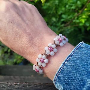 Geknoopte armband van donkerbruin koord met bloemetjes van rozenkwarts en roze rhinestone kralen.