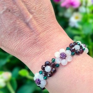 Goudkleurige RVS armband met verlengkettinkje, bloemetjes van granaat, rozenkwarts, rhinestone en Swarovski kraaltjes om de pols.